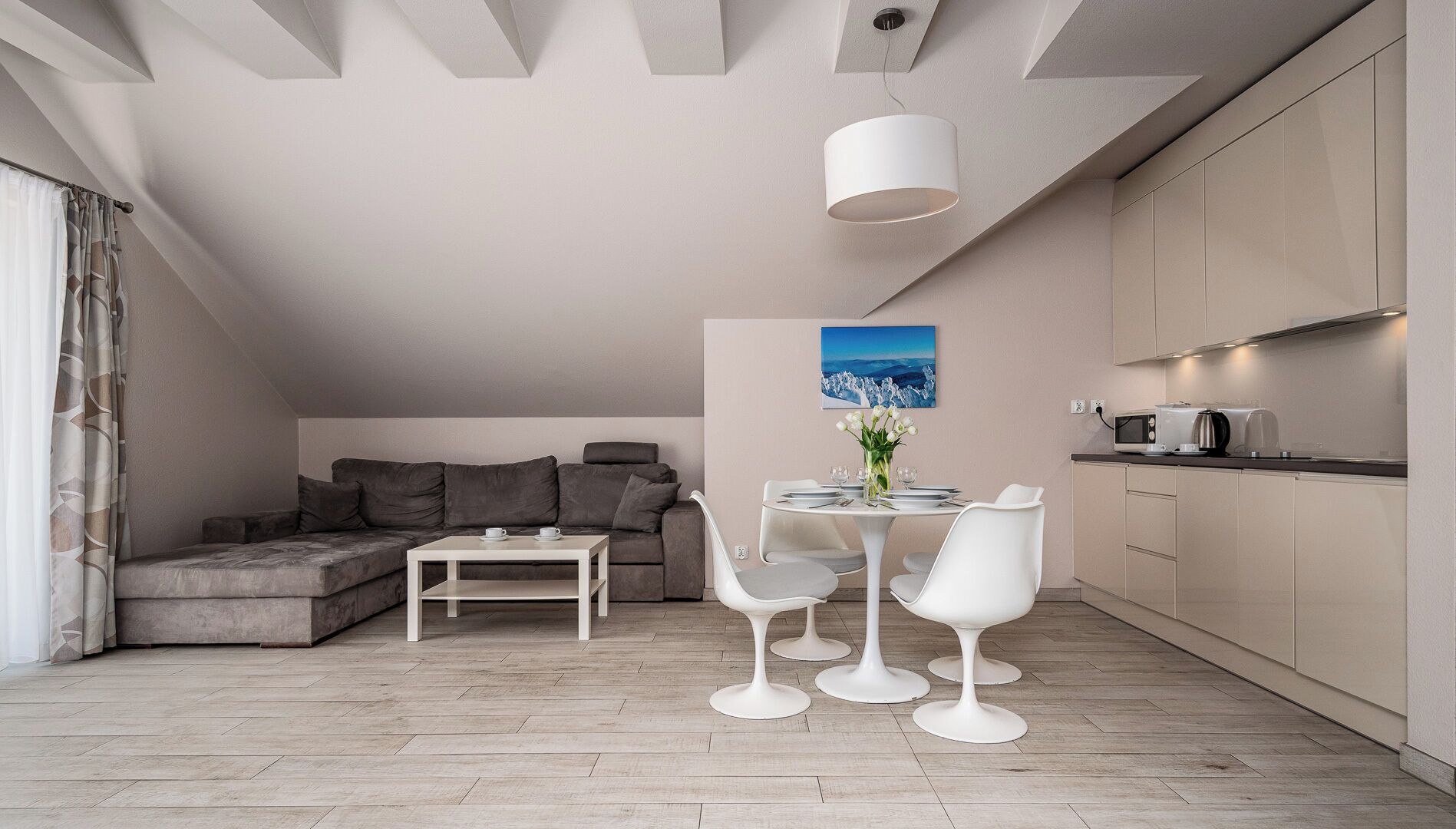 Moderni loft-tyylinen huoneisto, jossa on parvelle sijoitettu sänky, valkoisilla tuoleilla varustettu ruokailutila, mikroaaltouuni, ja suuri ikkuna.