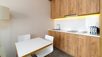 Una pequeña kitchenette con cubierta blanca, armarios de madera, un lavamanos y una mesa blanca con sillas.