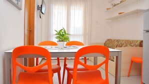 A dining area with a table, four orange chairs, a potted plant, and a window with sheer curtains. - Lovely Beachfront Apartment-beahost (San Michele al Tagliamento)