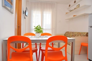 A dining area with a table, chairs, a potted plant, and a sofa in the background. - Lovely Beachfront Apartment-beahost (San Michele al Tagliamento)