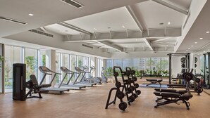 Une salle de sport moderne équipée de tapis de course, d’appareils de musculation et d’une grande fenêtre laissant entrer la lumière naturelle.
