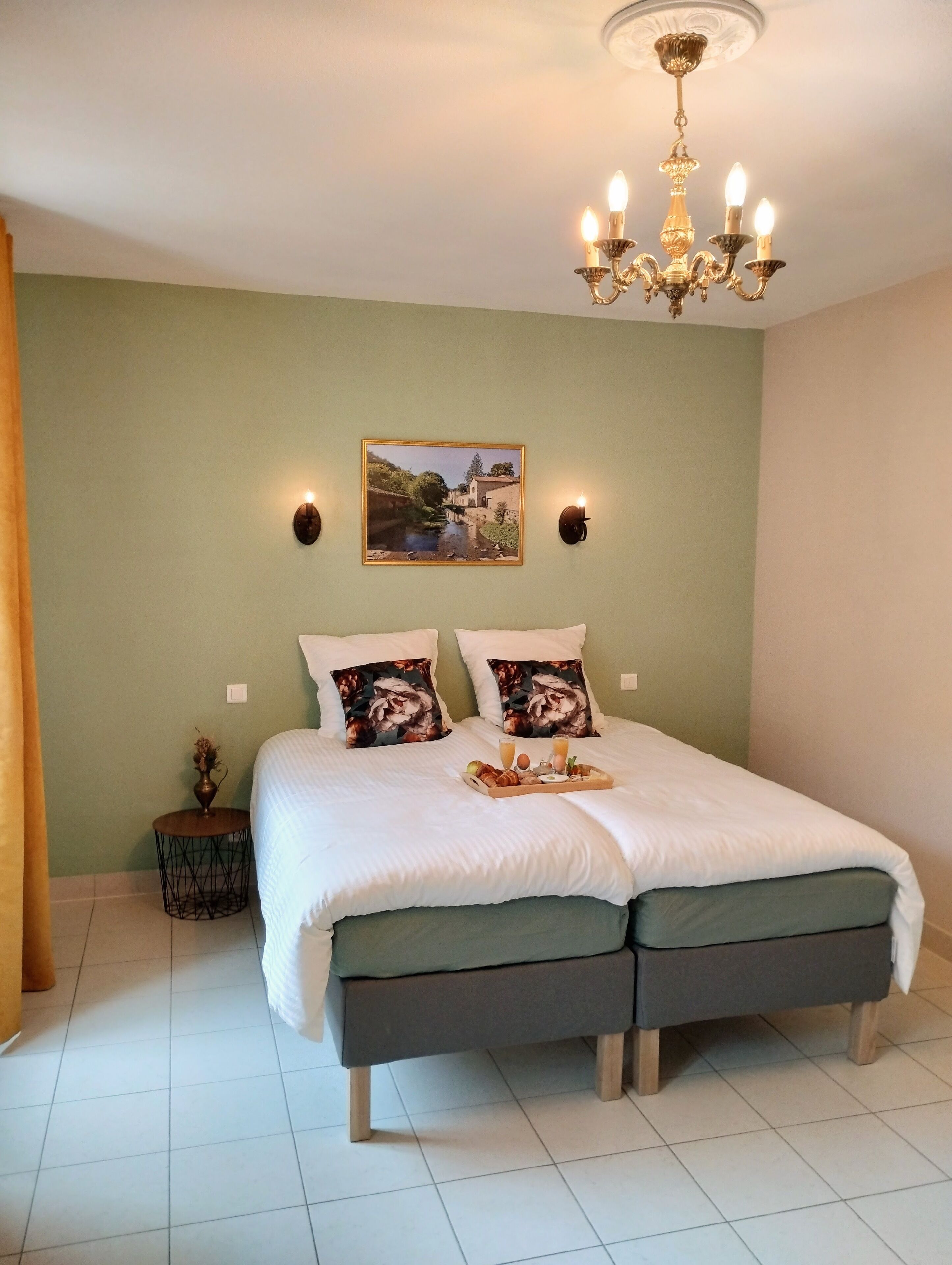 Un lit bien fait, avec un plateau de petit-déjeuner, un lustre et un tableau accroché au mur.