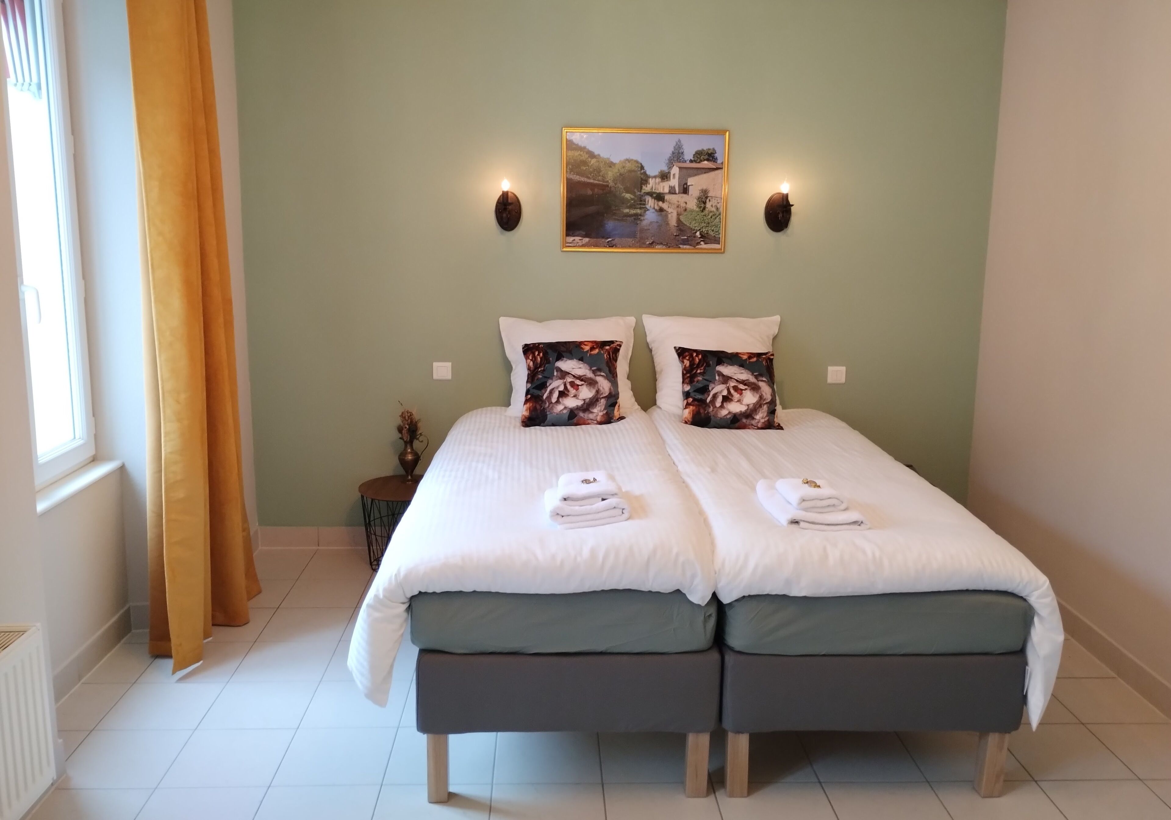 A double bed with matching pillows, a small bedside table, and a wall-mounted picture.