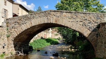 A stone bridge over a clear stream with buildings in the background.