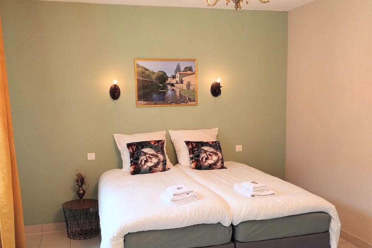 A double bed with a green upholstered headboard, two white pillows, and a decorative wall-mounted light fixture.