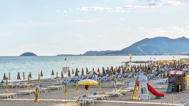A beach with rows of sun loungers and umbrellas, a children's play area, and a view of the sea and distant hills. - Amazing apartment in Loano with WiFi (Loano)