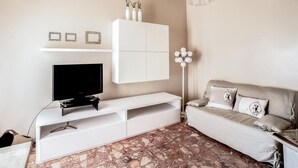 A living room with a TV on a white stand, a sofa, and a floor lamp. - Amazing apartment in Loano with WiFi (Loano)