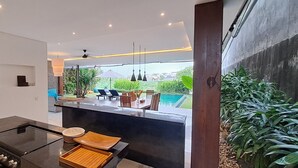 Una cocina moderna con estufa integrada, un comedor con vista a la piscina y un amplio ventanal que da a zonas verdes.