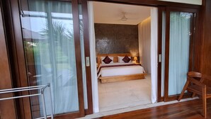 Un dormitorio con una cama, una silla de madera y un ventanal corredero que da a un balcón con plantas.