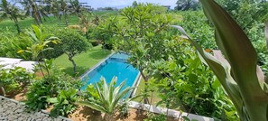 A rectangular pool surrounded by lush greenery and palm trees. - Villa Nesara (Munggu)