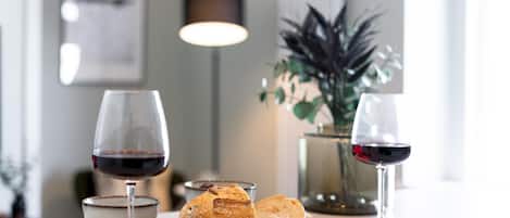 A table with two wine glasses, a bowl, and a loaf of bread on a wooden board.