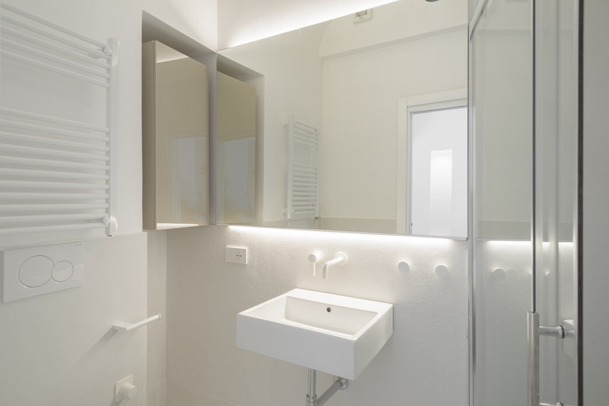 A modern bathroom with a white sink, a mirror, and a glass shower enclosure.