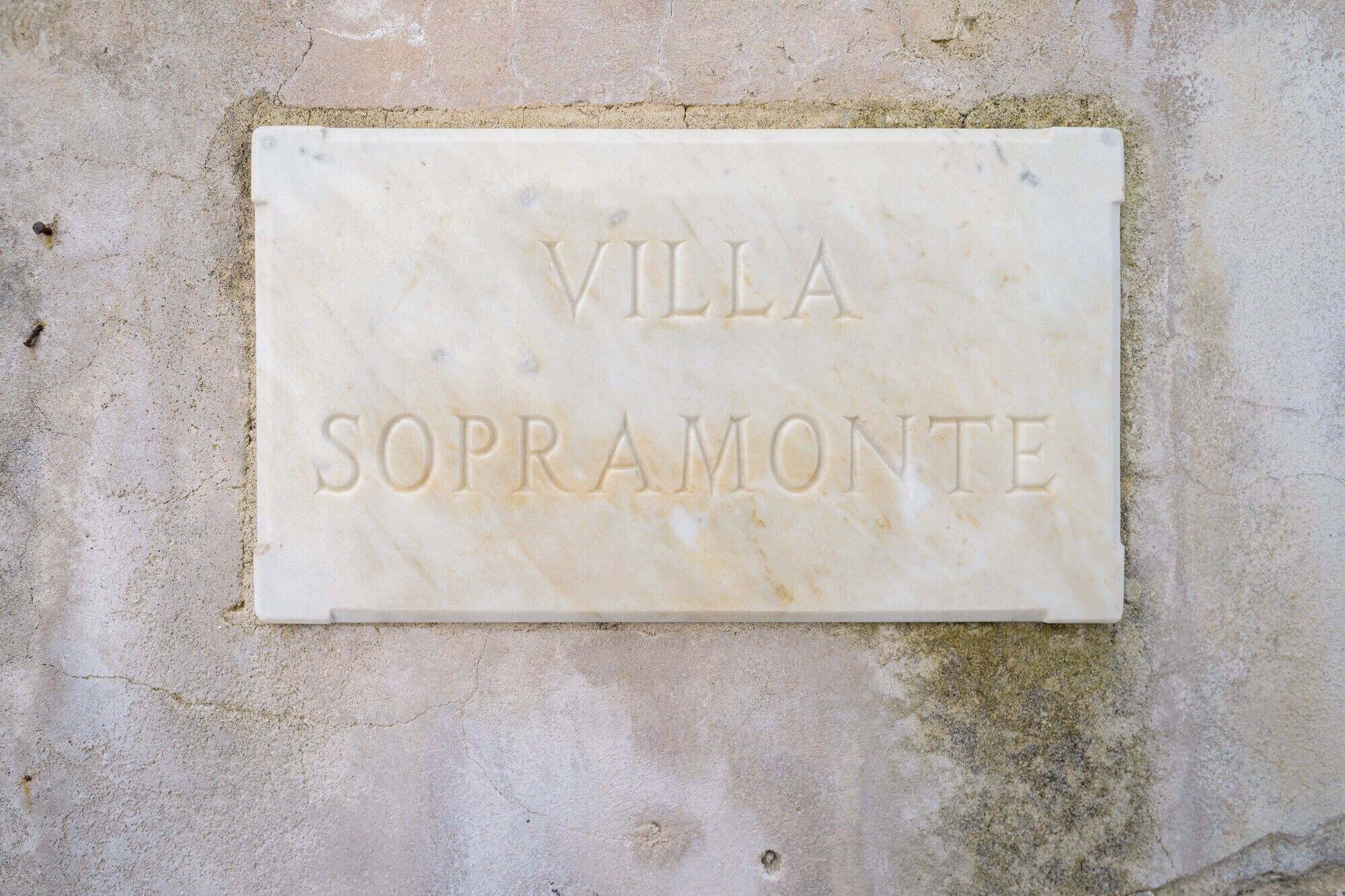 A marble plaque with the inscription "VILLA SOPRAMONTE" on a textured wall.