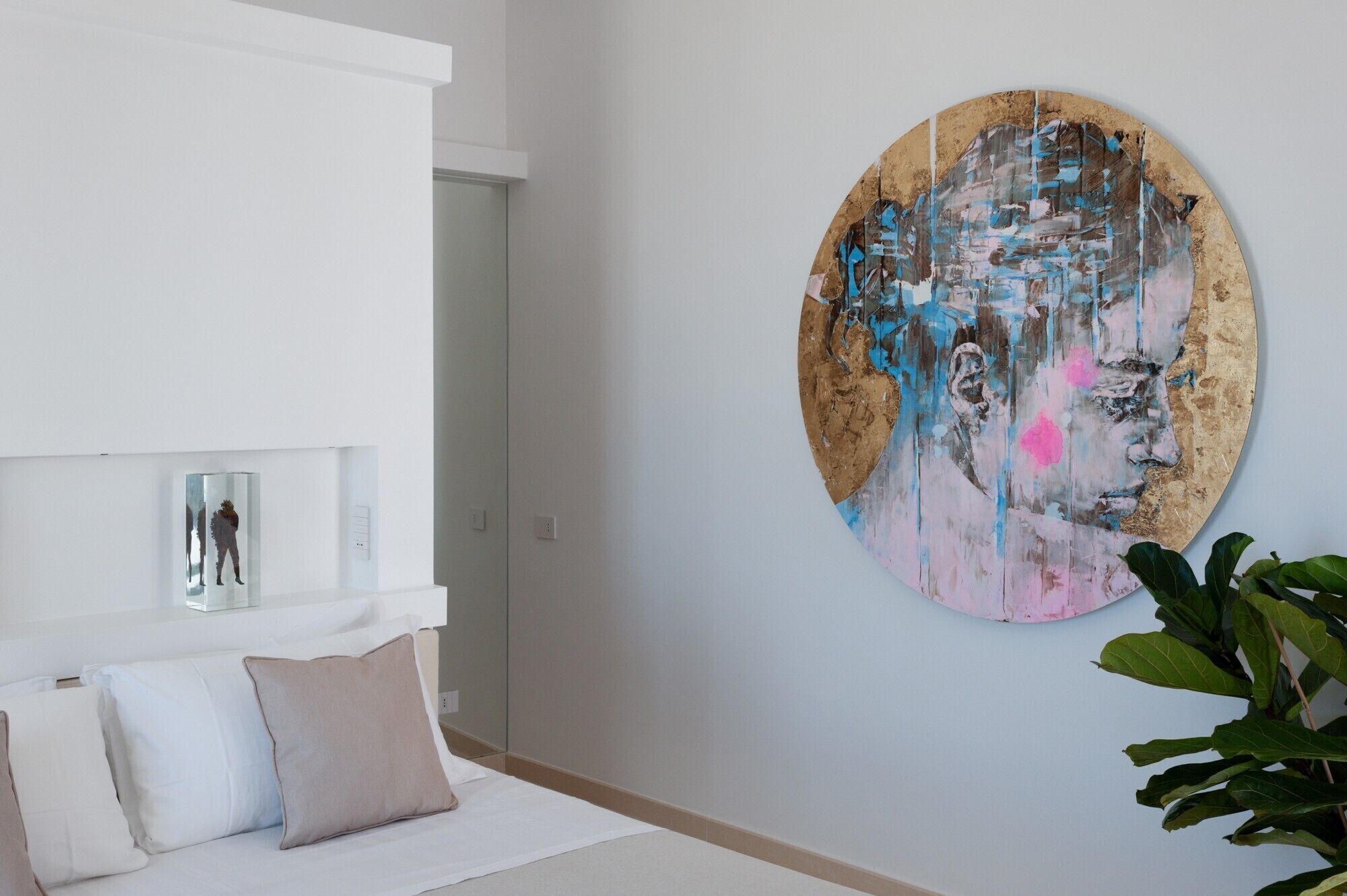 A modern living room with a white sofa, a large abstract painting, and a potted plant.