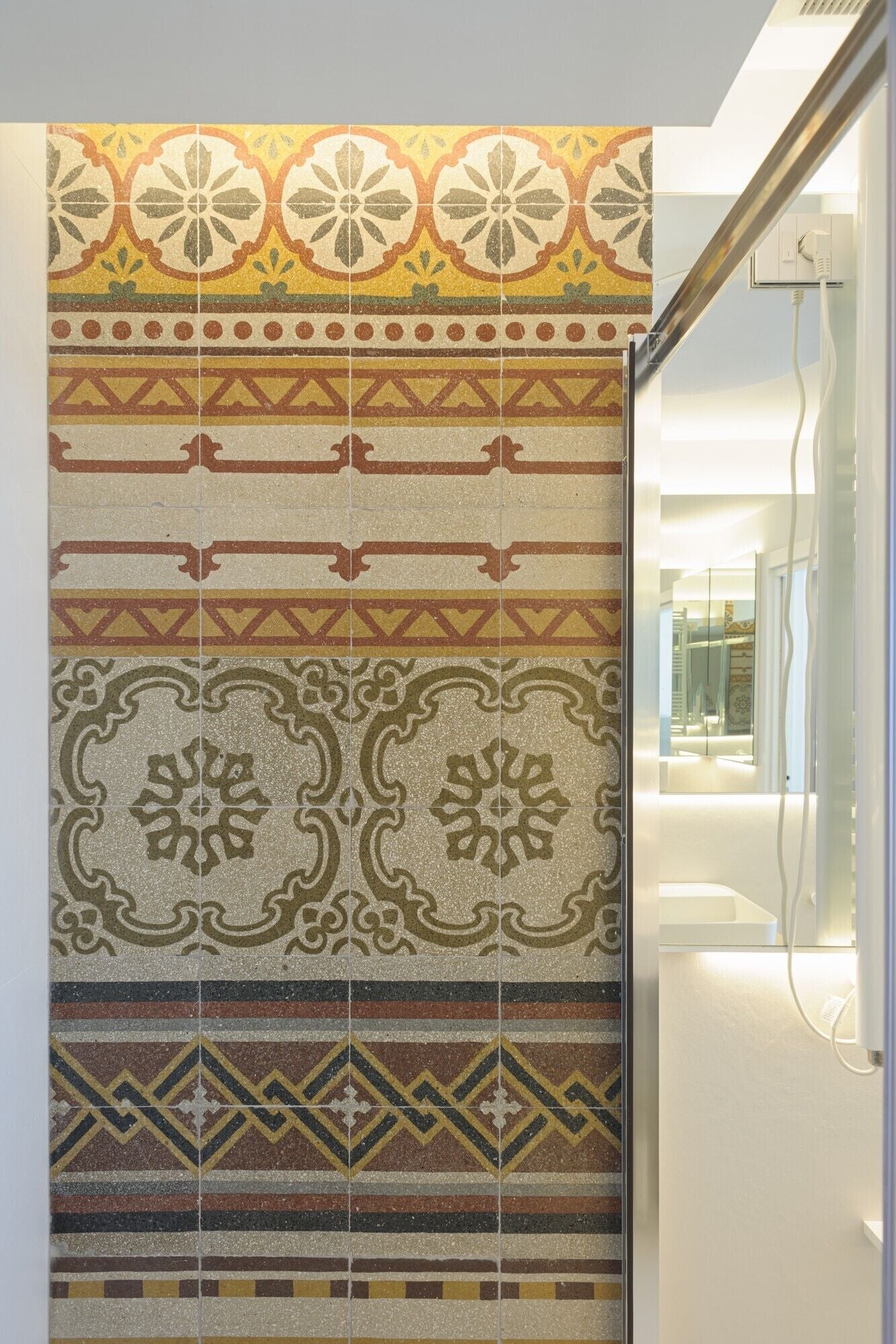 Paredes com padrão geométrico e floral, um interior moderno com divisória de vidro, e uma tomada elétrica visível.