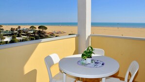 A balcony with a view of the beach, a round table with chairs, and a potted plant. - Elegant and Bright Studio Apartment Near the Beach (San Michele al Tagliamento)