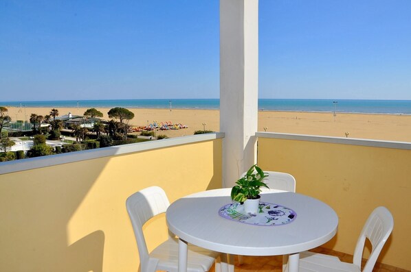 A balcony with a view of the beach, a round table with chairs, and a potted plant. - Elegant and Bright Studio Apartment Near the Beach (San Michele al Tagliamento)