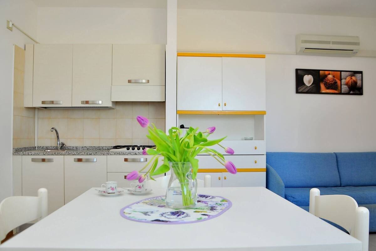 Una cucina moderna con mobili bianchi, un piano cottura a gas e un'area pranzo con tavolo apparecchiato per due.