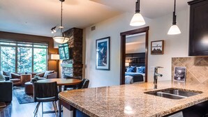 A modern kitchen with granite countertops, a Bosch dishwasher, and a dining area with a round table and chairs. - Three Bears Hydeaway at Stoneridge (Canmore)