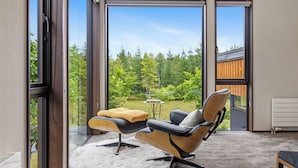 Una habitación moderna con un gran ventanal corredera que da a un jardín, un sillón cómodo con una manta y una pequeña mesa redonda.