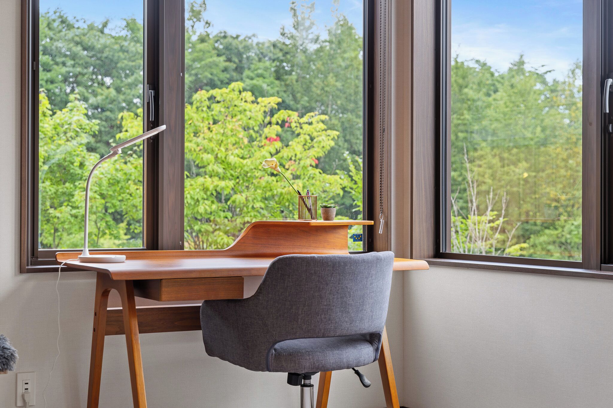 A modern desk with a chair, a desk lamp, and a small potted plant.