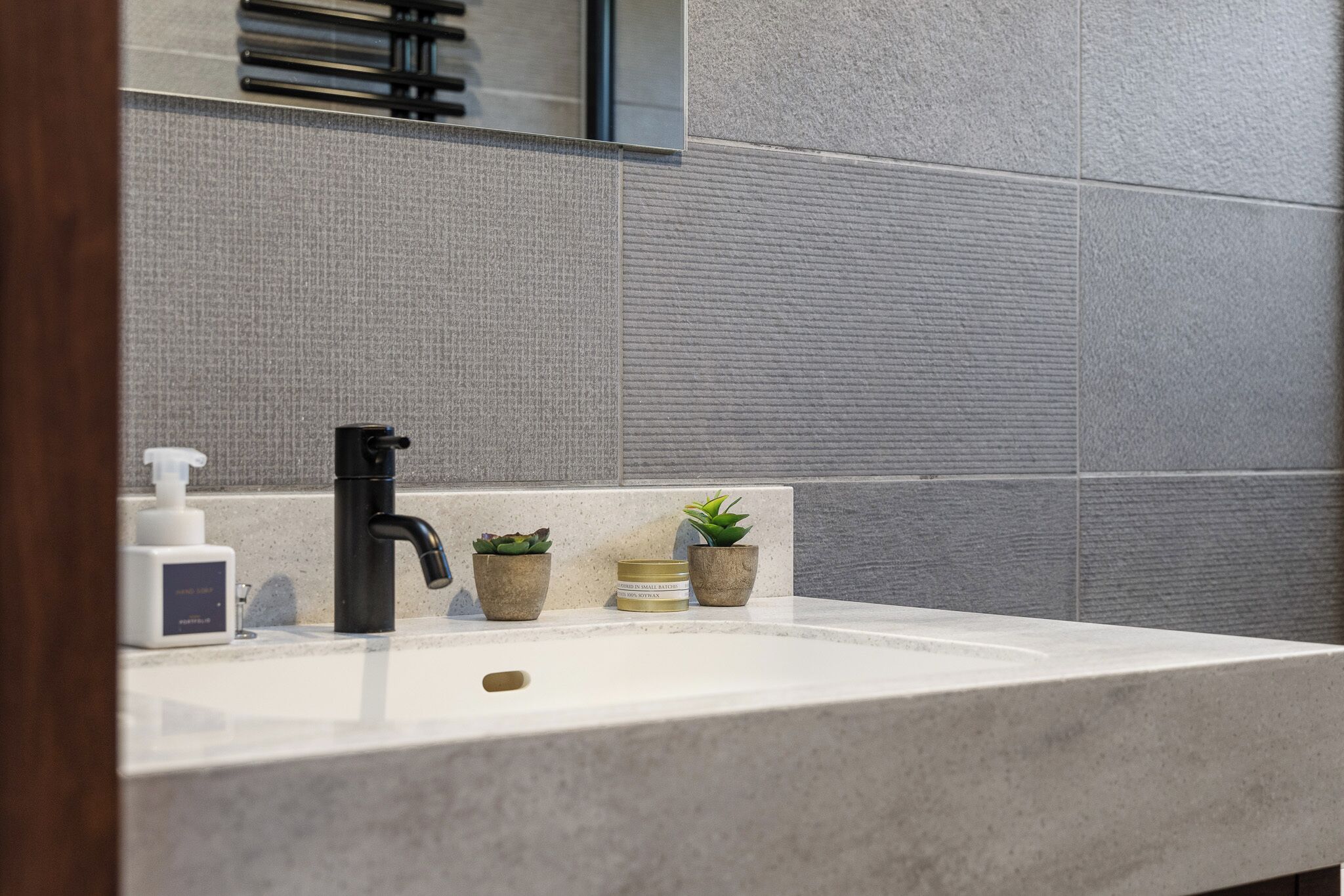 A bathroom with a white sink, black faucet, and two potted plants.