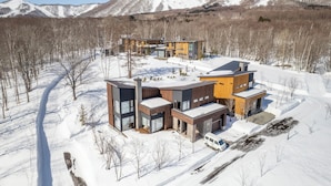 Una casa moderna de varios pisos con un paisaje nevado y montañas al fondo.