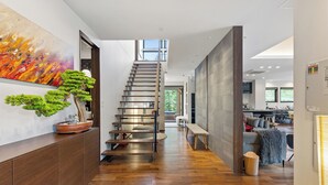 Un interior moderno con una escalera de madera, un comedor y una sala de estar con un sofá y un banco.