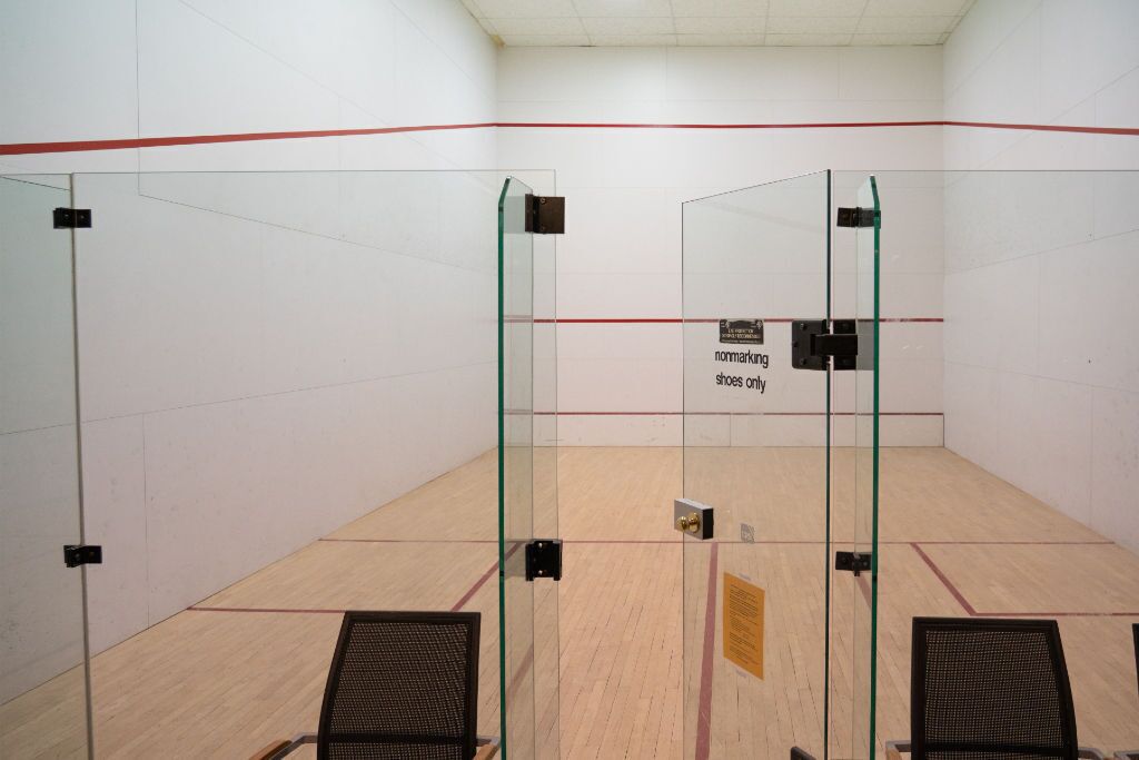 A squash court with glass doors, a wooden floor, and a sign indicating shoe-only access.