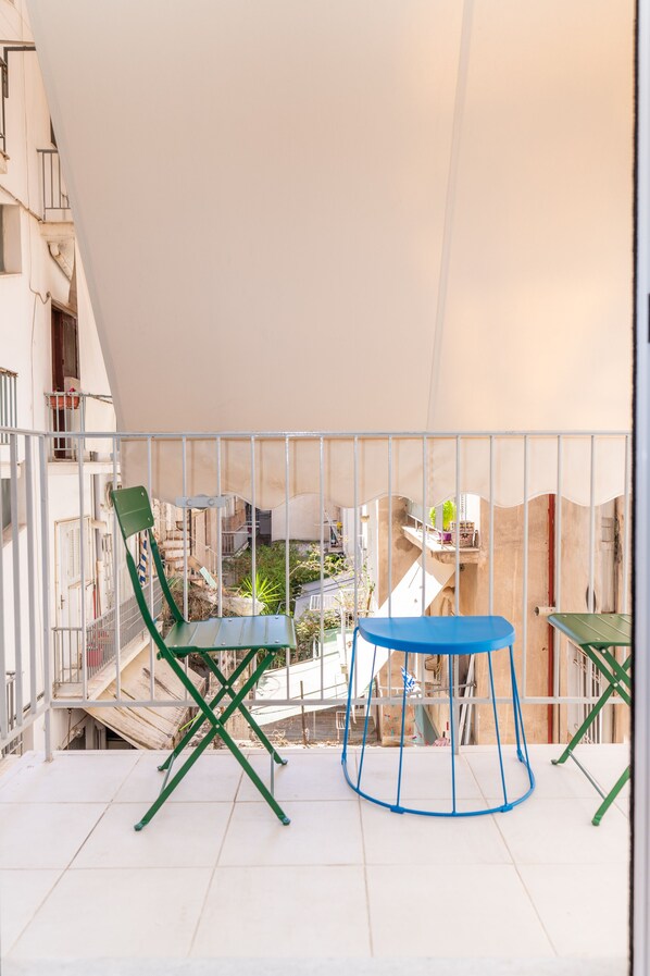Un balcon doté d’un plafond blanc, de chaises vertes et bleues, et d’une petite table ronde.