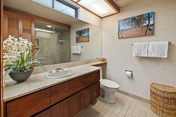 Un baño con tocador de madera, un lavabo, un inodoro y un espejo grande. Hay dos toallas colgadas en la pared y una cesta en el suelo.