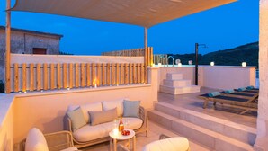 A rooftop terrace with a sofa, a table with a bottle and glasses, and sun loungers. - La Mirage Villa (Kournas)