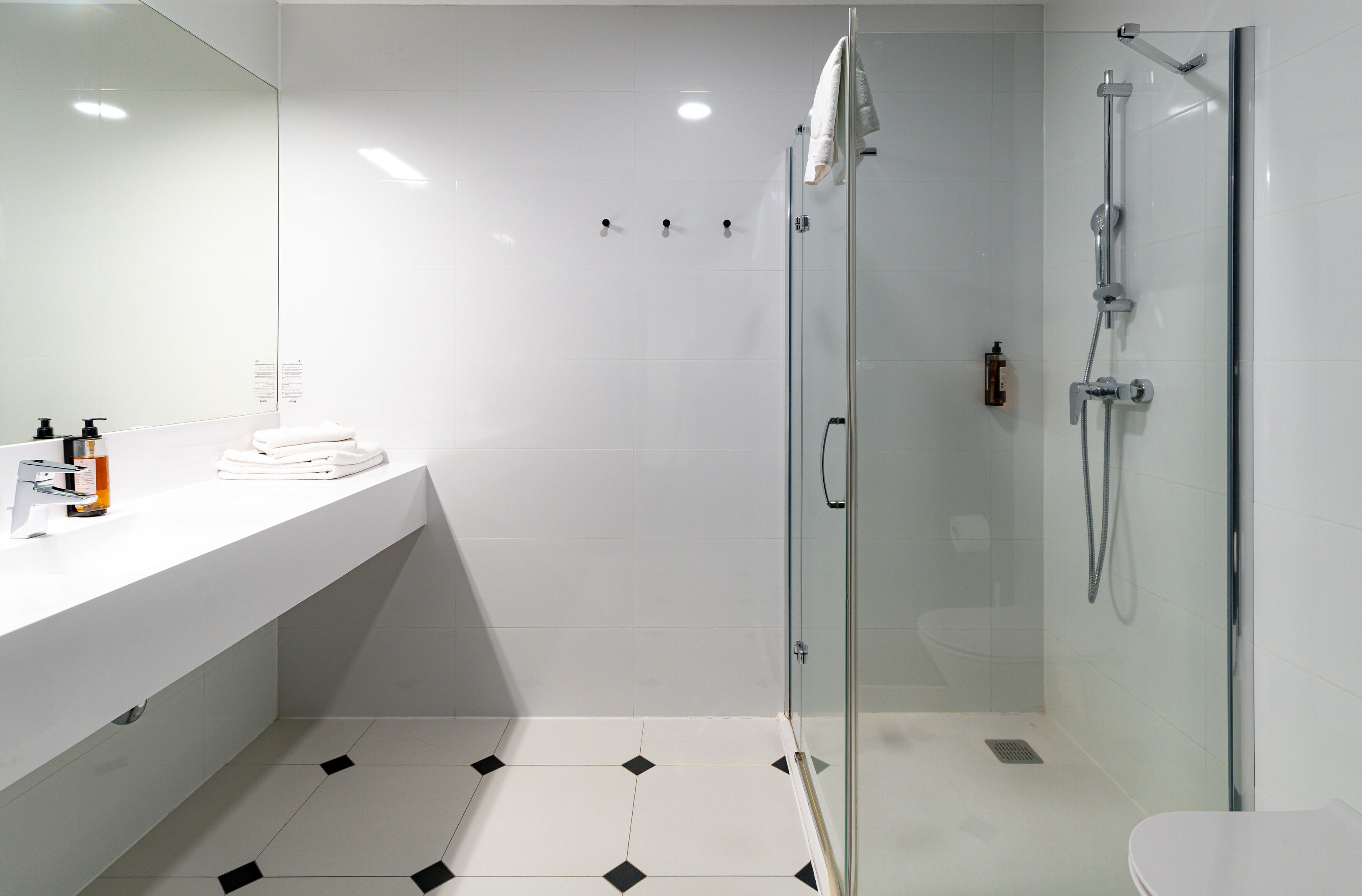 A modern bathroom with a glass shower enclosure, a white sink with toiletries, and a tiled floor.