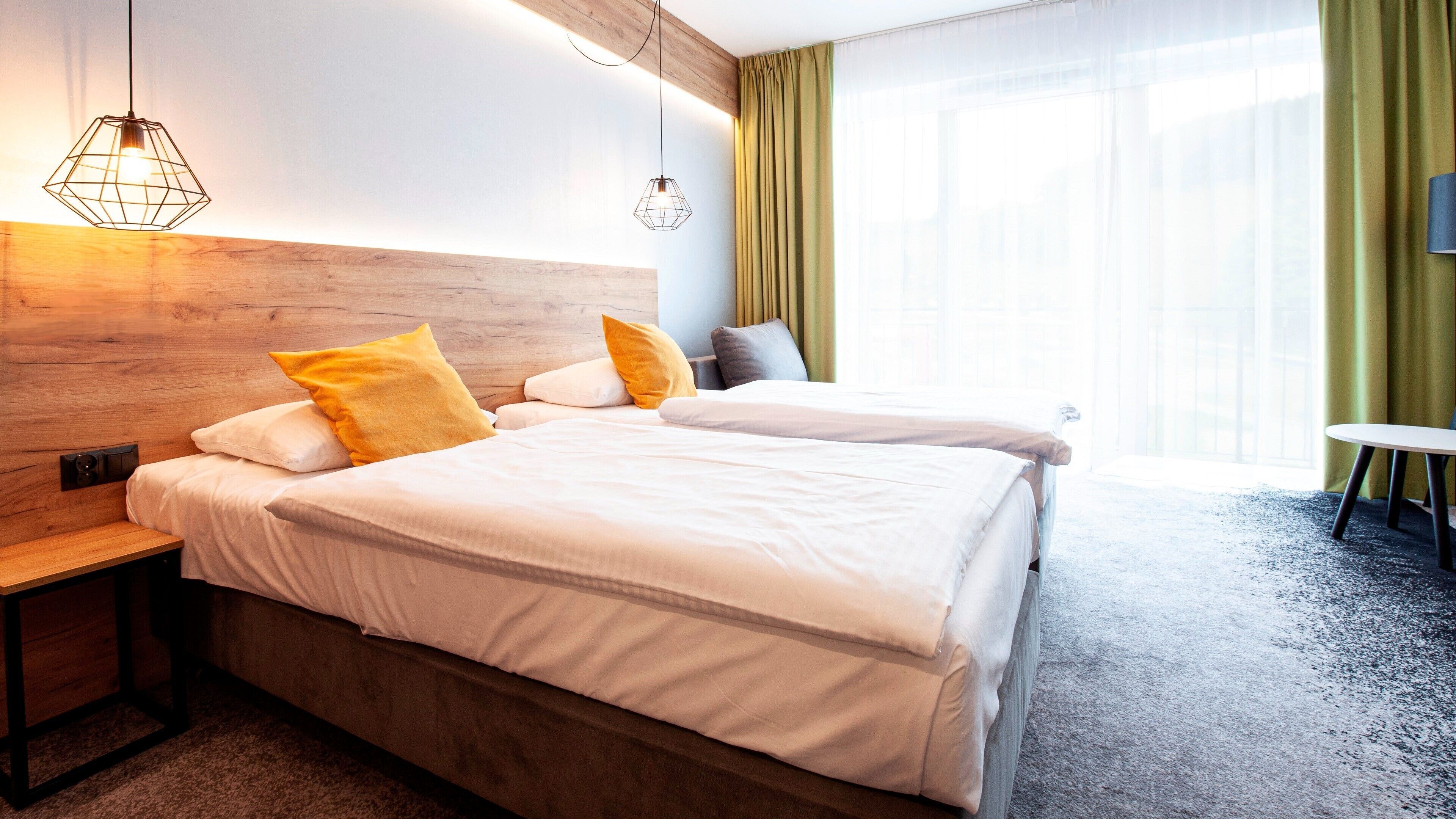 Habitación de hotel con cabecera de madera, cama con ropa de cama blanca, dos mesitas de noche y una pequeña mesa redonda.