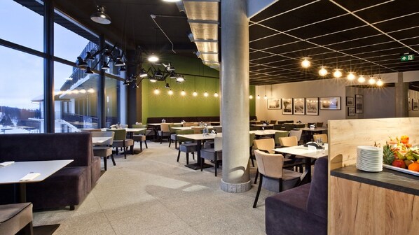 Un restaurante moderno con techos altos, ventanas amplias y diferentes opciones de asientos.