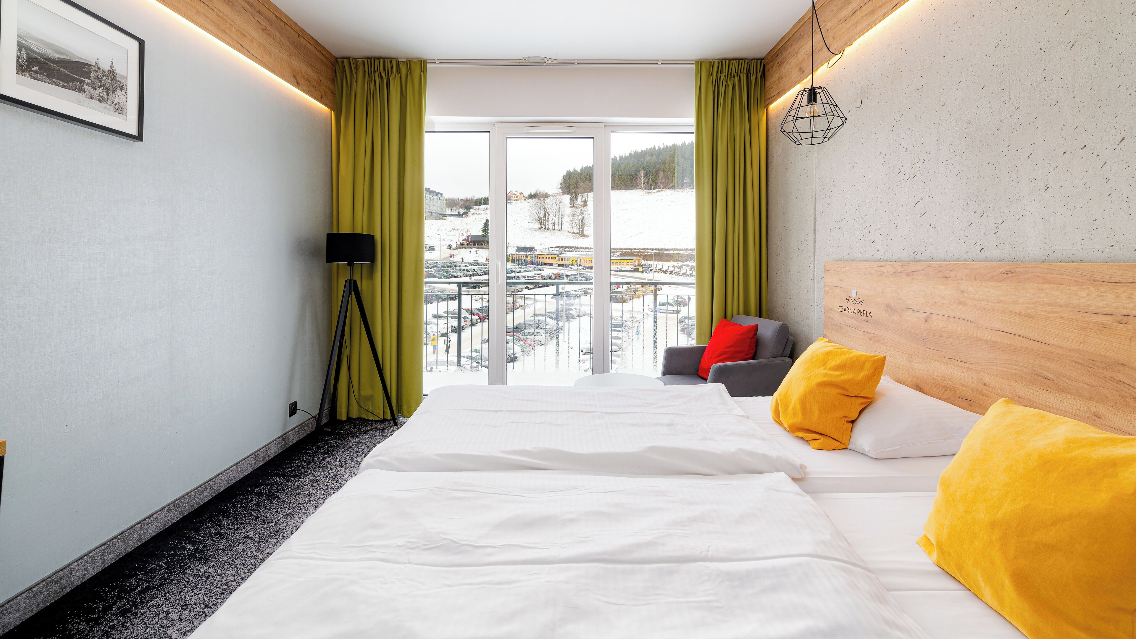 Habitación de hotel con cama, sofá, lámpara de pie y vista a un paisaje nevado a través del ventanal.