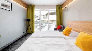 Habitación de hotel con cama, sofá, lámpara de pie y vista a un paisaje nevado a través del ventanal.