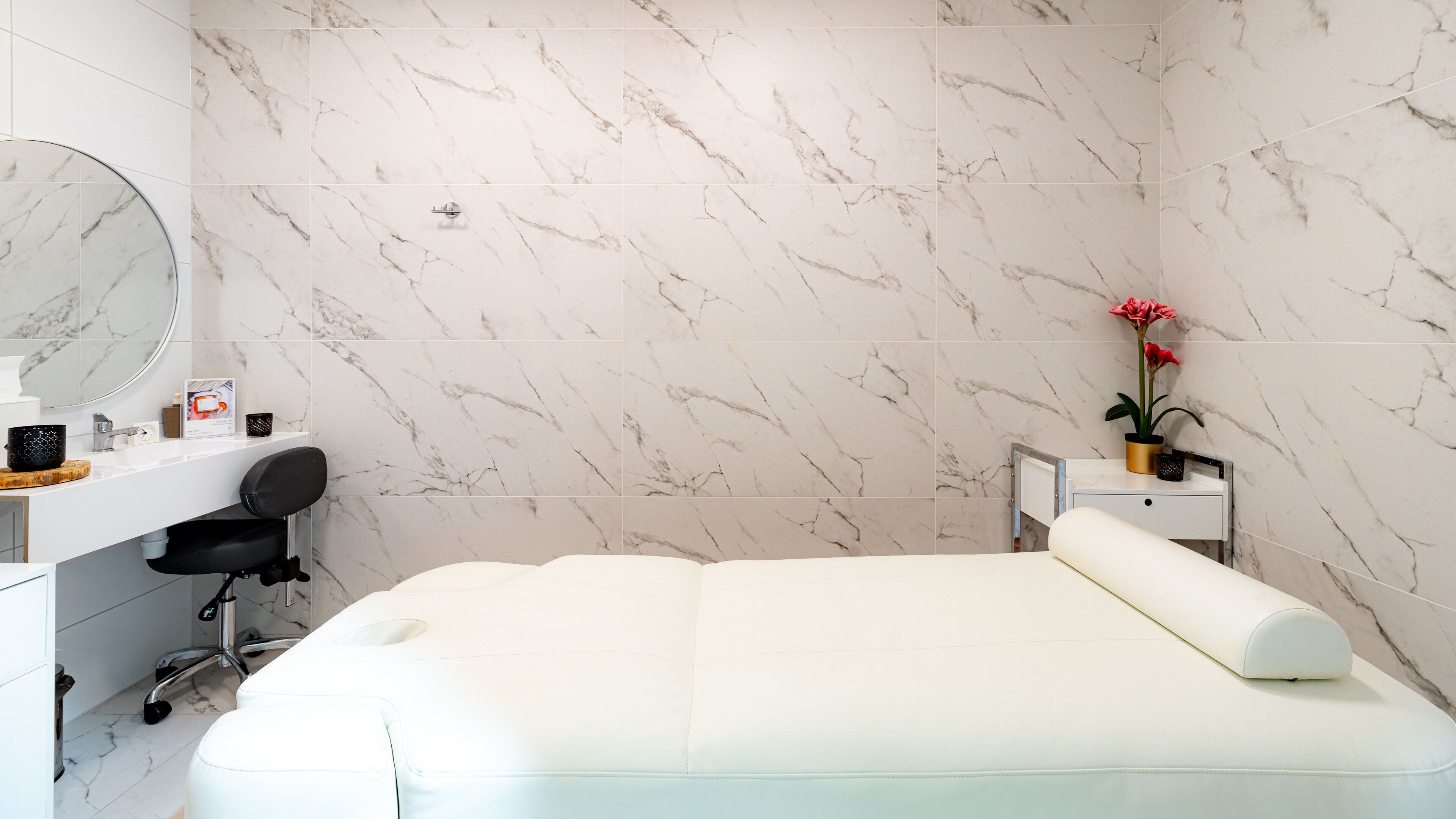 A modern bathroom with a marble wall, a sink, a chair, and a bed with a white mattress.