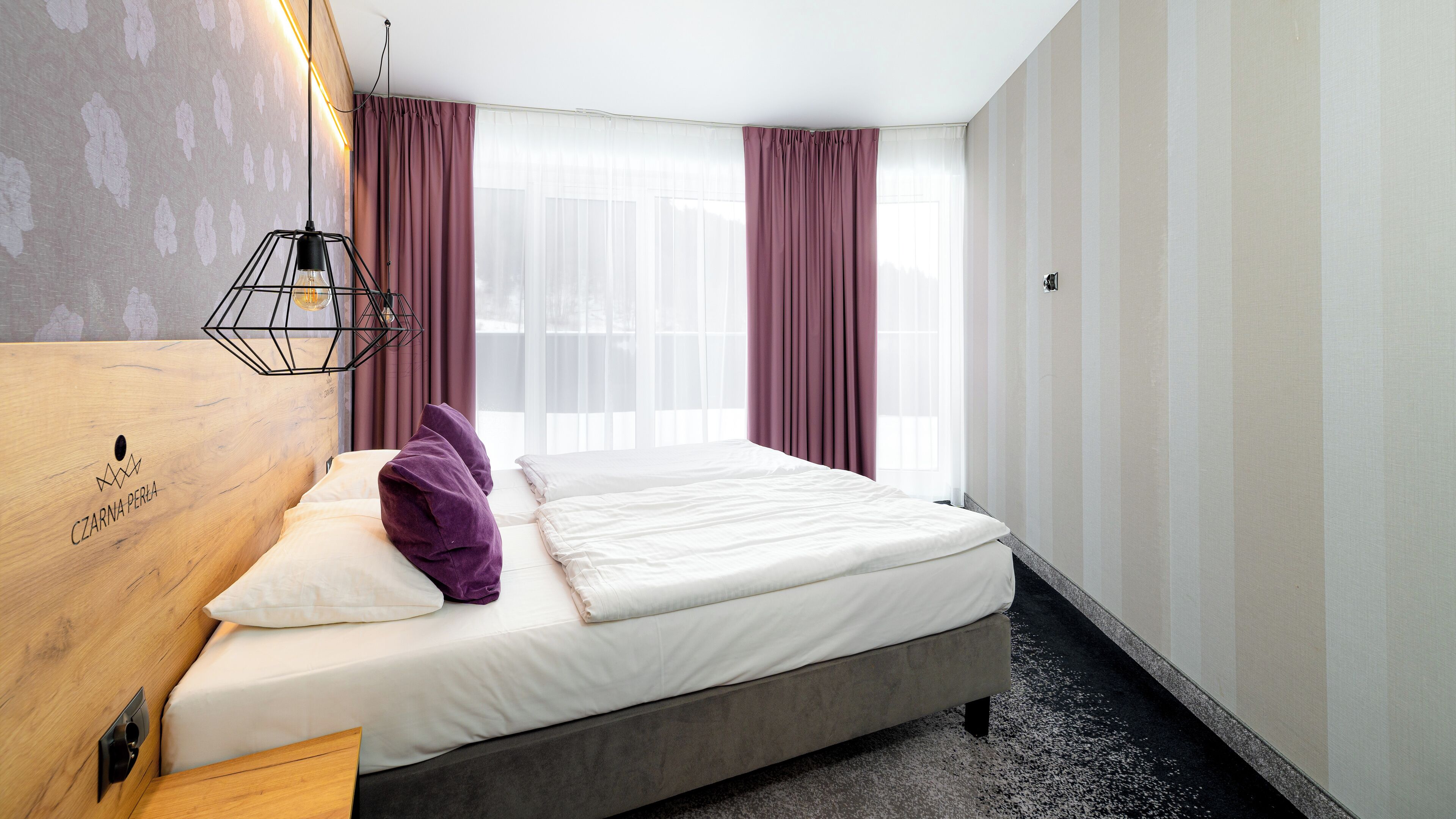 Ett hotellrum med en säng, en träpanel som huvudgavel, ett nattduksbord och ett fönster med gardiner.