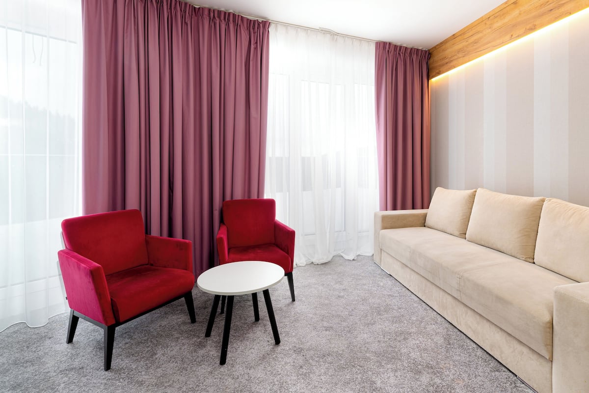 Una habitación moderna con un sofá beige, dos sillones rojos y una pequeña mesa blanca.