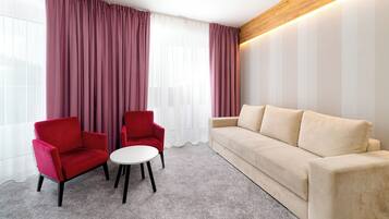 Una habitación moderna con un sofá beige, dos sillones rojos y una pequeña mesa blanca.