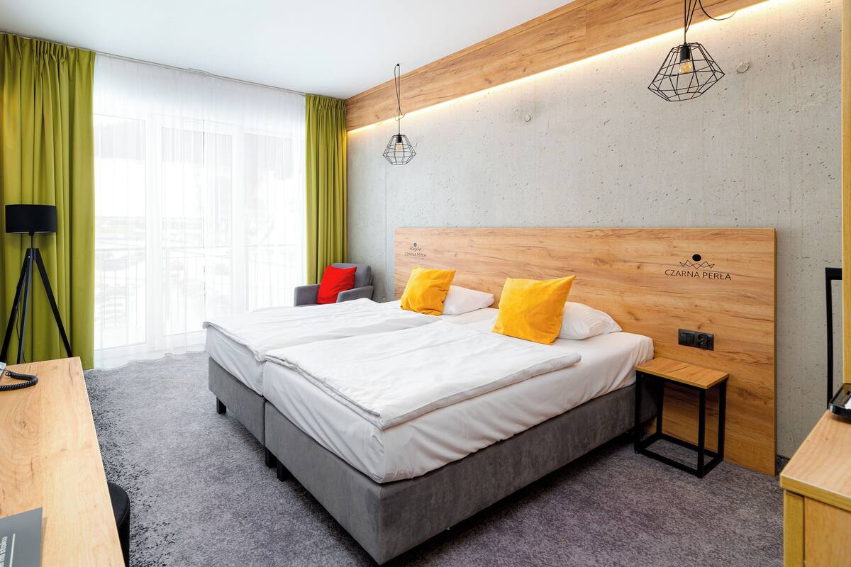 Una habitación de hotel moderna con una cama grande, dos mesitas de noche, un escritorio, una silla y una cámara en la pared.