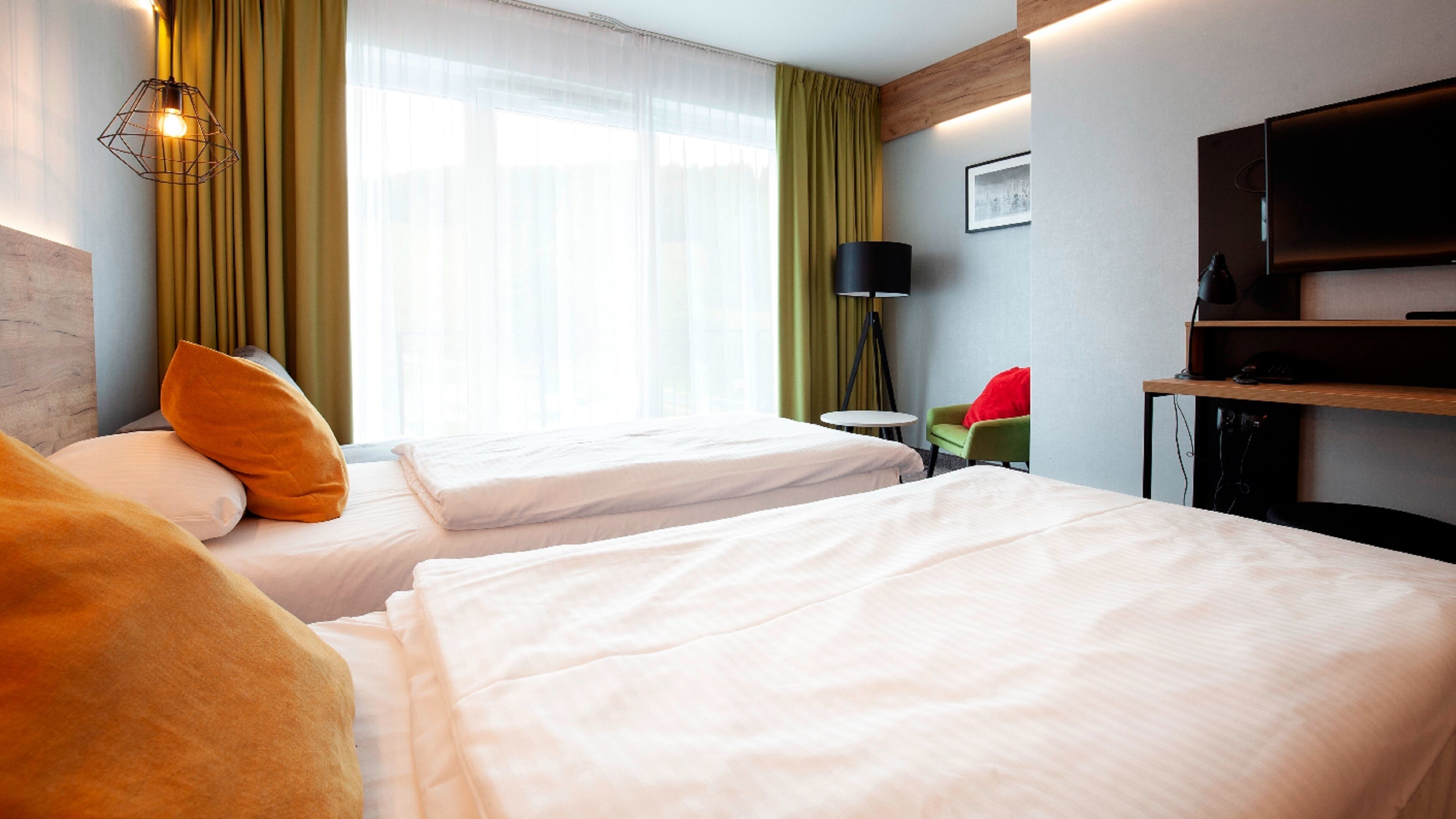 Une chambre d’hôtel avec deux lits, un bureau, une chaise, une télévision et une fenêtre avec des rideaux.