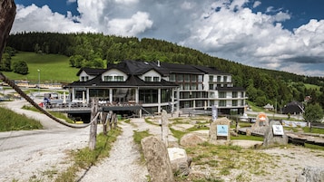 Un hotel moderno con una amplia fachada de vidrio, ubicado en una zona montañosa con vistas a densos bosques.