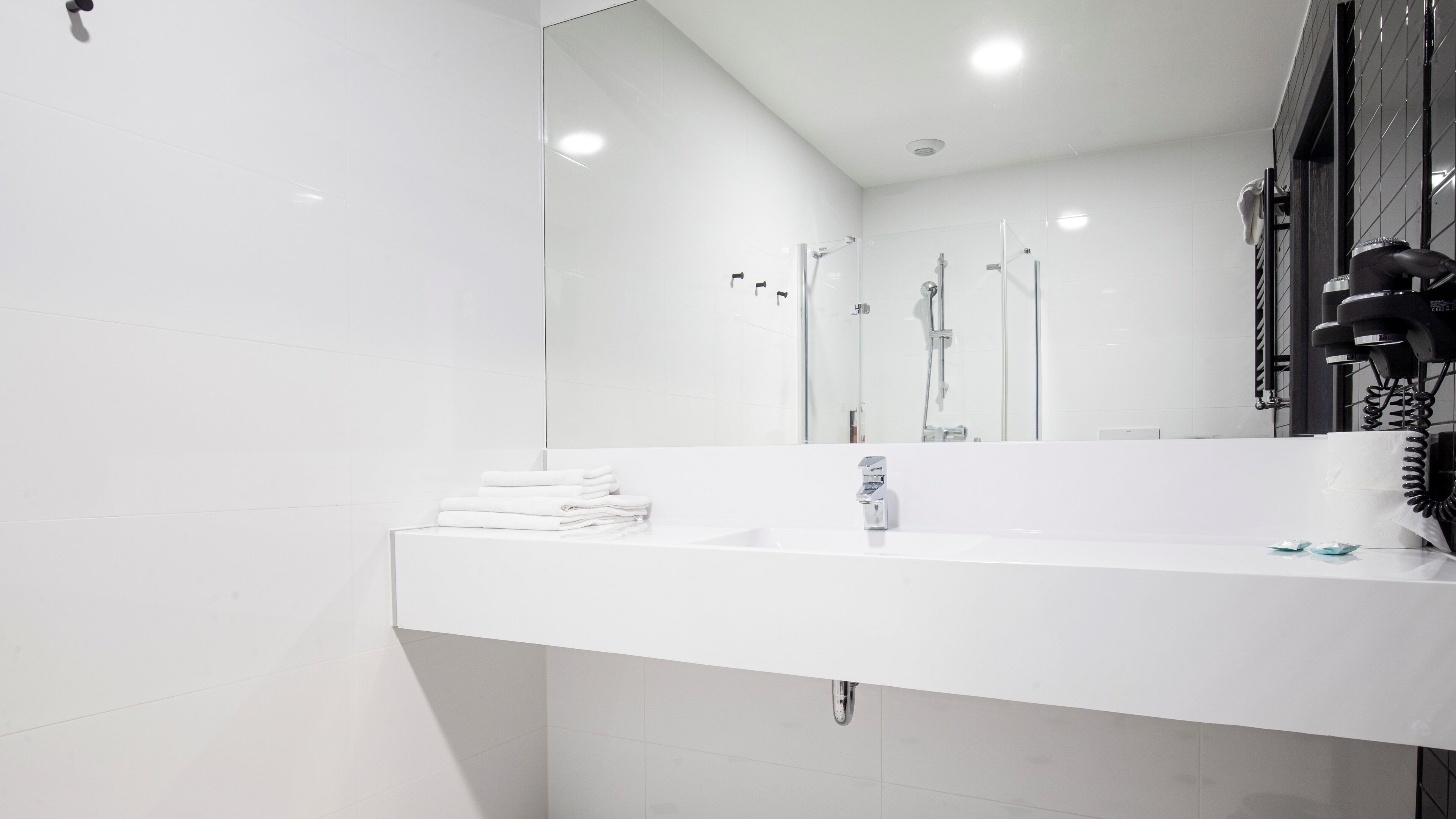 Un baño moderno con un espejo grande, lavamanos blanco y zona de ducha con paredes de vidrio.