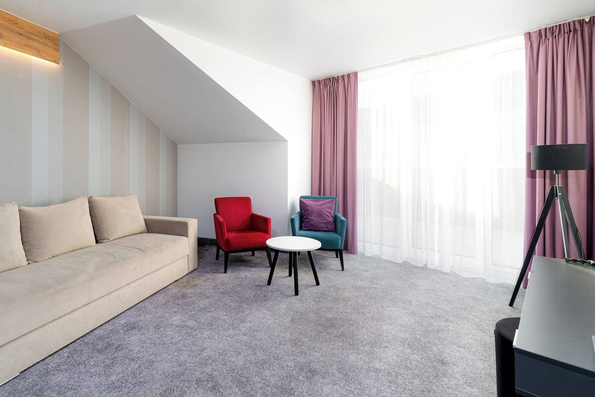 Una habitación de hotel moderna con sofá, dos sillones, una mesita y una lámpara de pie.
