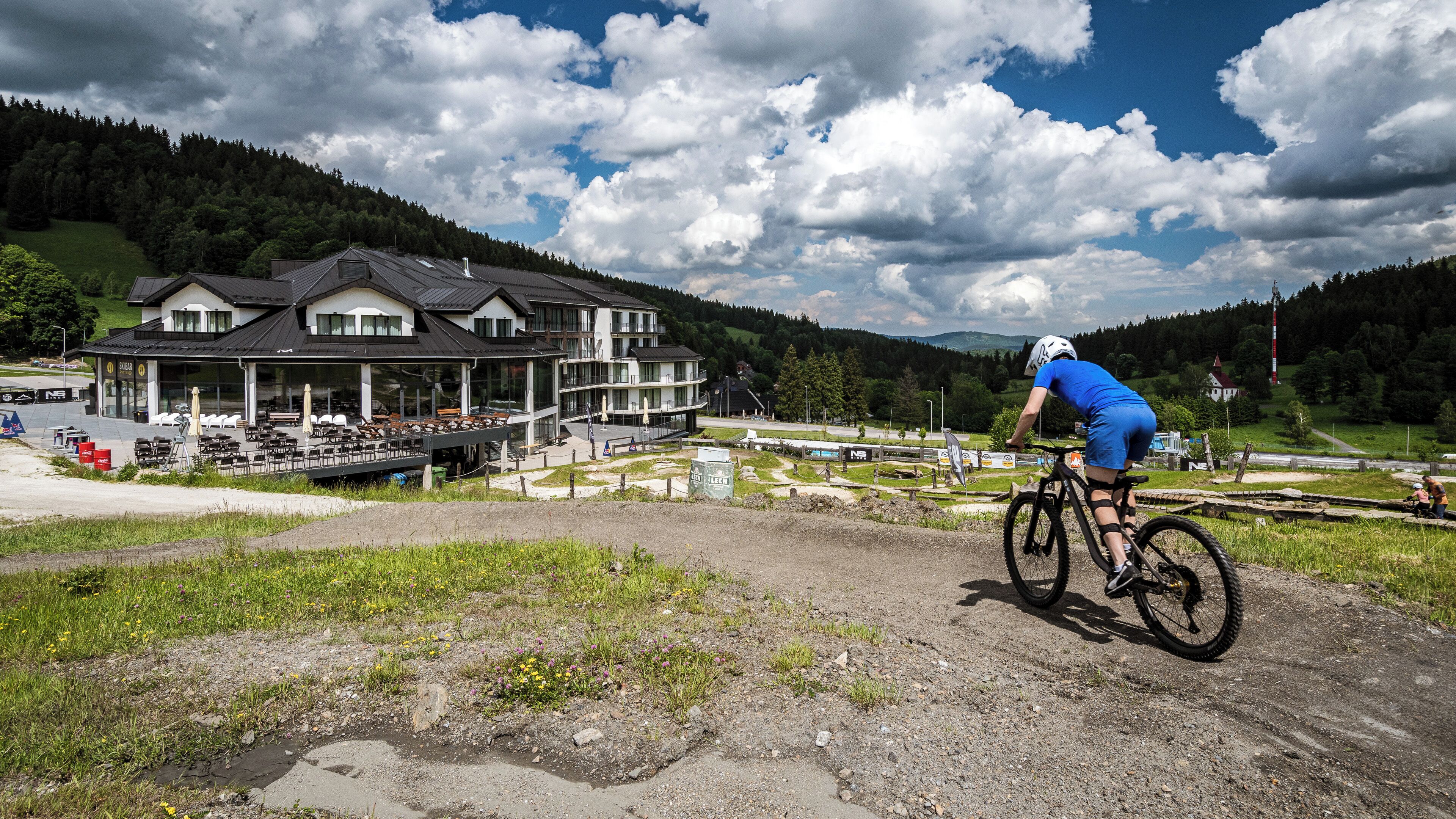 A cyclist on a dirt path with a building in the background.