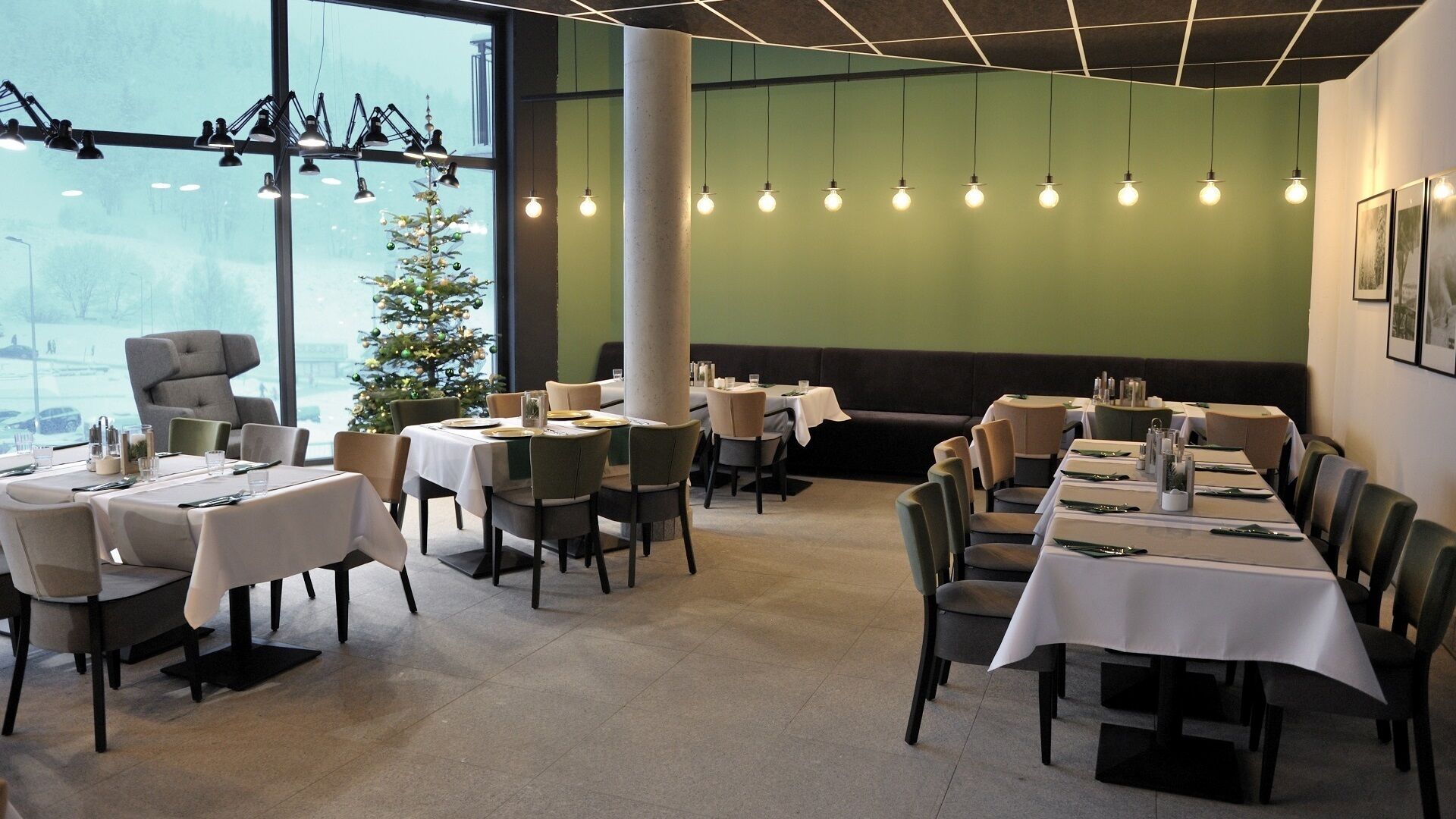 A restaurant with tables set for dining, a Christmas tree, and hanging light bulbs.
