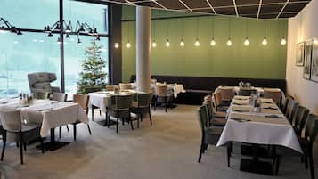 A restaurant with tables set for dining, a Christmas tree, and hanging light bulbs.