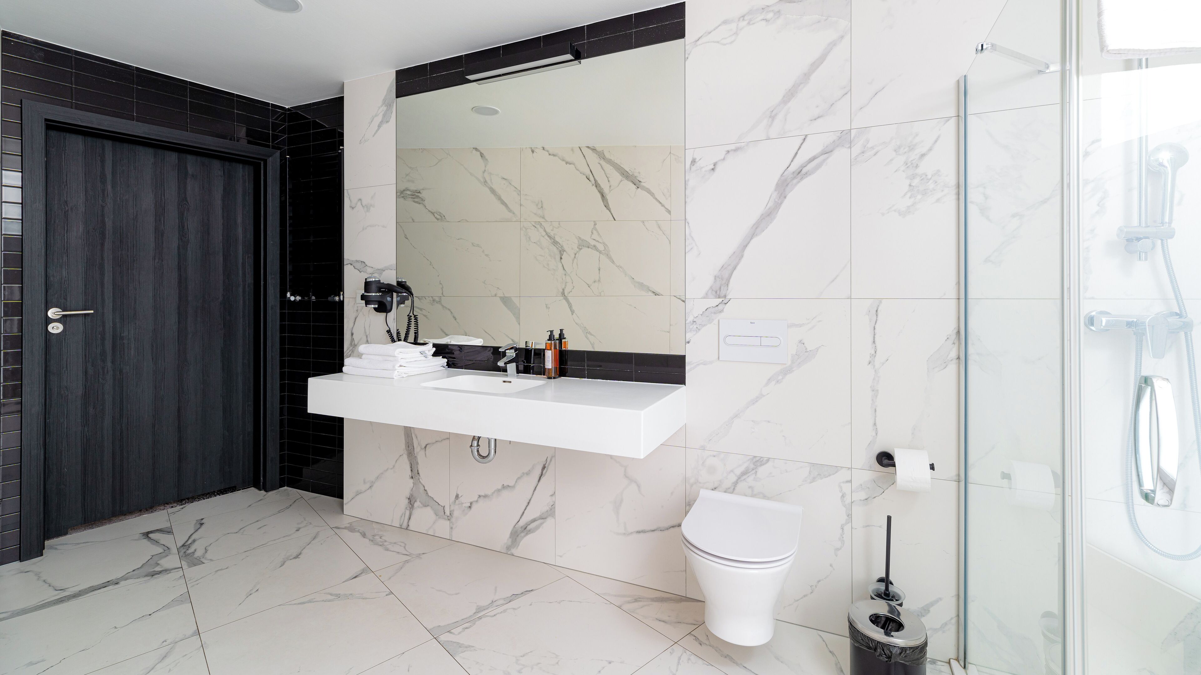 Ein modernes Badezimmer mit Waschbecken, Spiegel und Toilette in Weiß, Marmorfliesen und einer Duschkabine aus Glas.